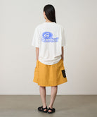 Rear view of a model wearing a white Gramicci '82 Tee with a blue graphic and yellow skort on a light tone background.