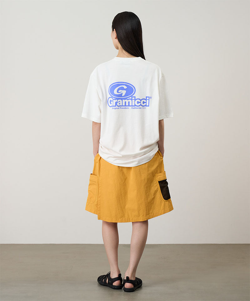Rear view of a model wearing a white Gramicci '82 Tee with a blue graphic and yellow skort on a light tone background.