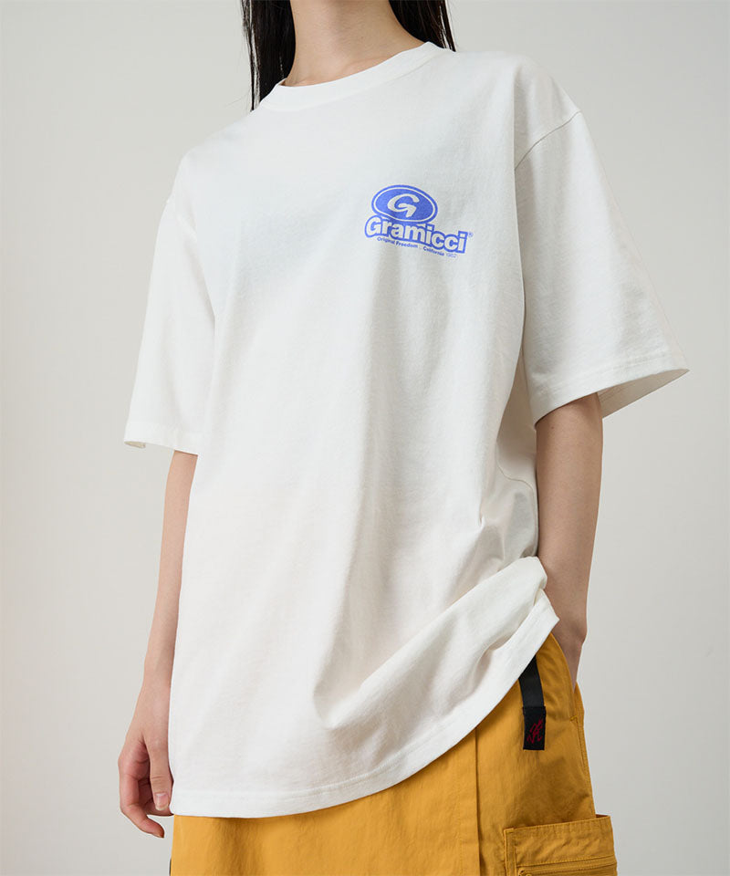 Model wearing a Gramicci white '82 Tee with blue graphic against a light tone background.