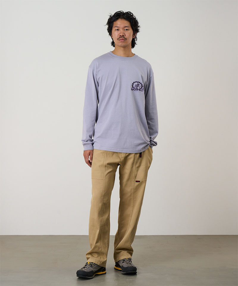 Model wearing a lavender Gramicci Equipped For Dirt L/S Tee with a a Gramicci gear graphic graphic and olive shorts on a light tone background.