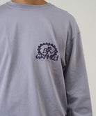 Model wearing a Gramicci lavender Equipped For Dirt L/S Tee with a Gramicci gear graphic graphic against a light tone background.