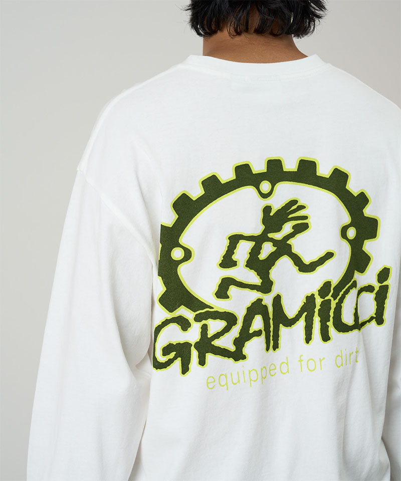 Back view of a model wearing a Gramicci white Equipped For Dirt L/S Tee with green graphic against a light tone background.