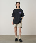 Model wearing a vintage black Gramicci Equipped For Dirt Tee with a purple graphic and beige shorts on a light-tone background.