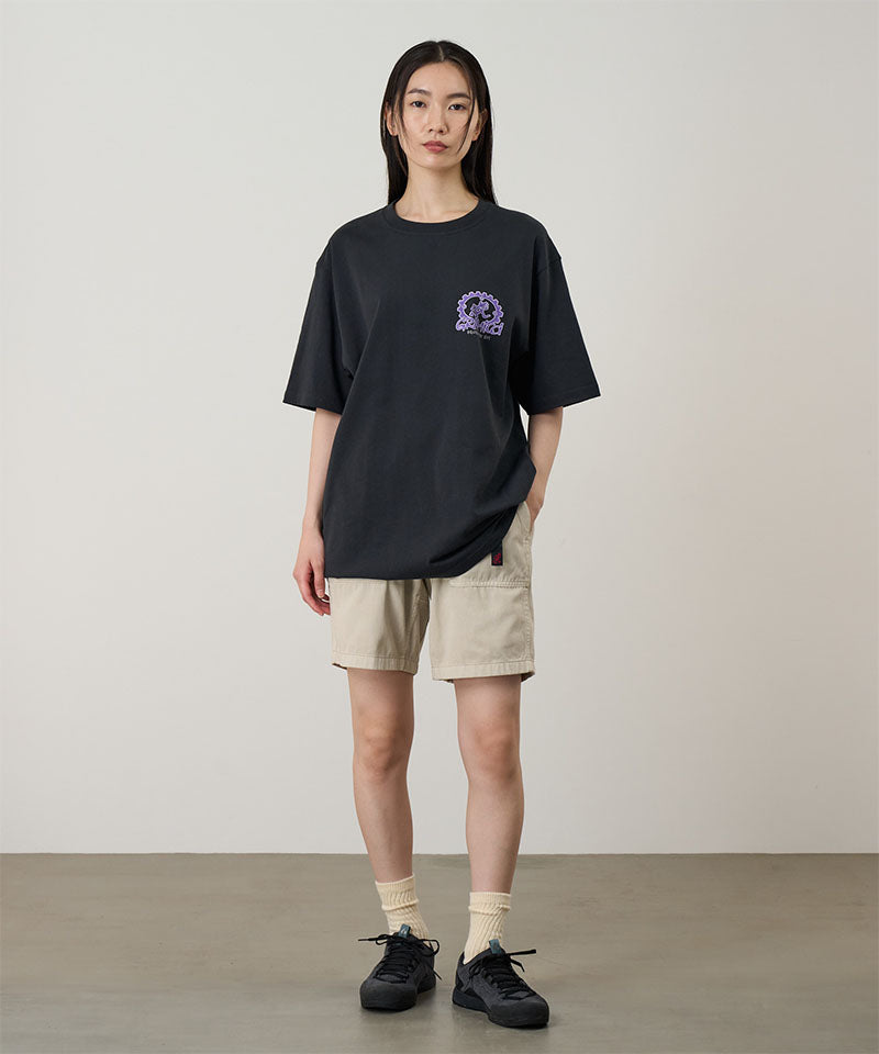 Model wearing a vintage black Gramicci Equipped For Dirt Tee with a purple graphic and beige shorts on a light-tone background.