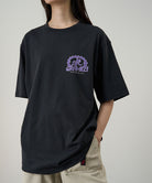 Model wearing a Gramicci vintage black Equipped For Dirt Tee with a purple graphic against a light-tone background.
