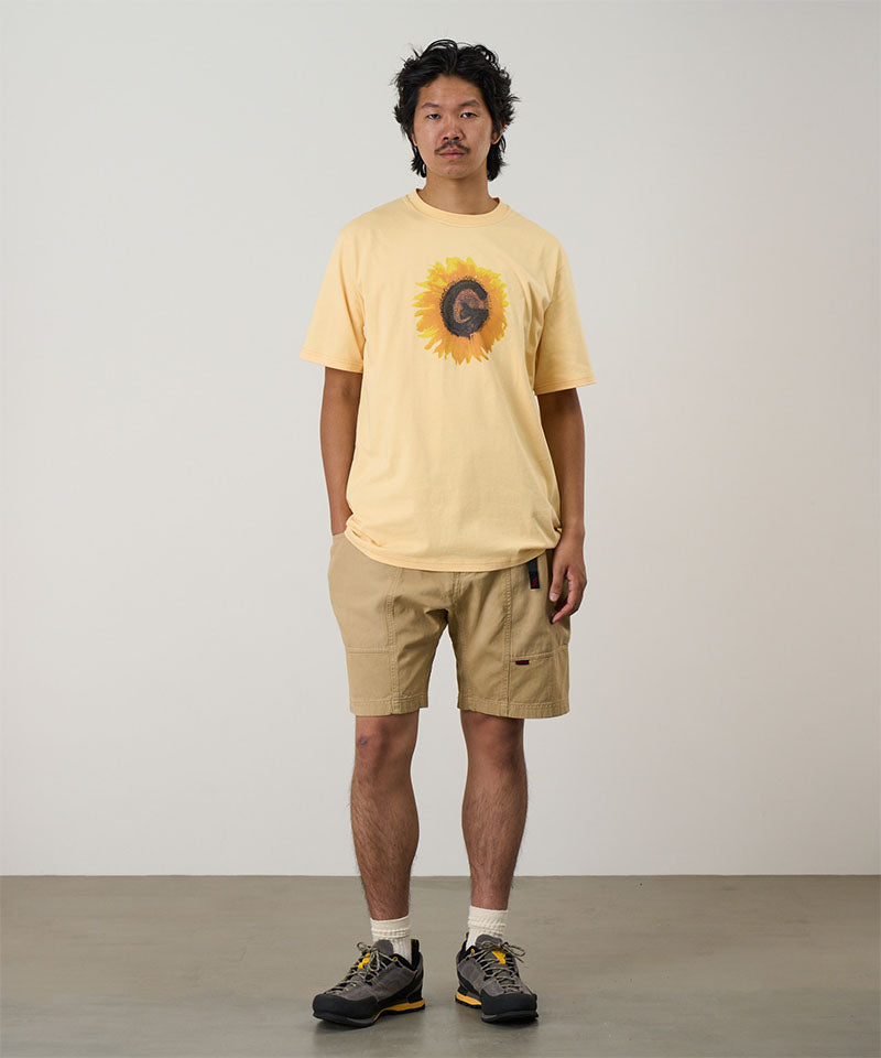 Model wearing a mango Gramicci G-Flower Tee with a sunflower graphic and beige shorts on a light tone background.