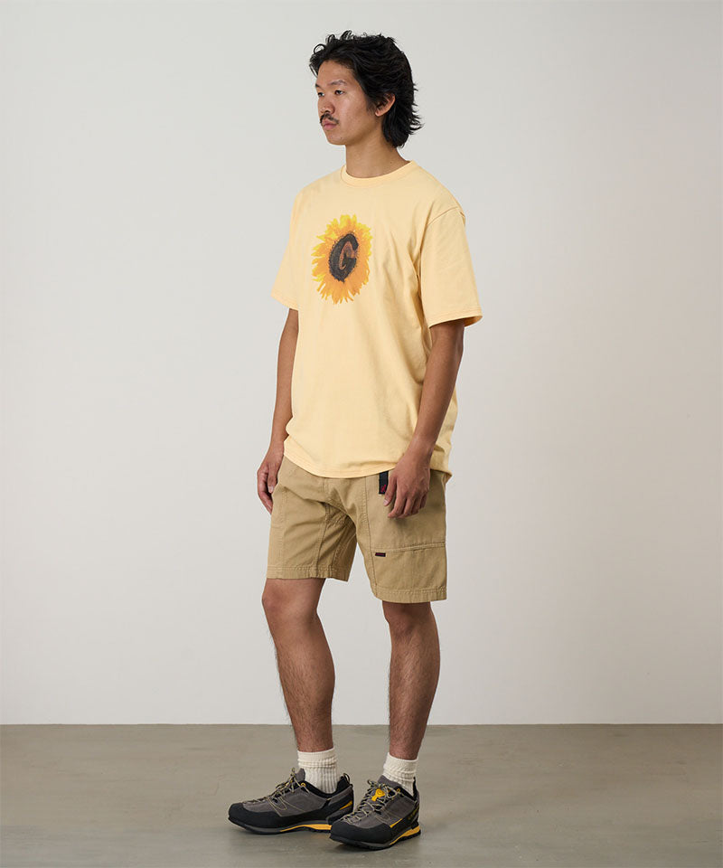 Model wearing a mango Gramicci G-Flower Tee with a sunflower graphic and beige shorts on a light tone background.