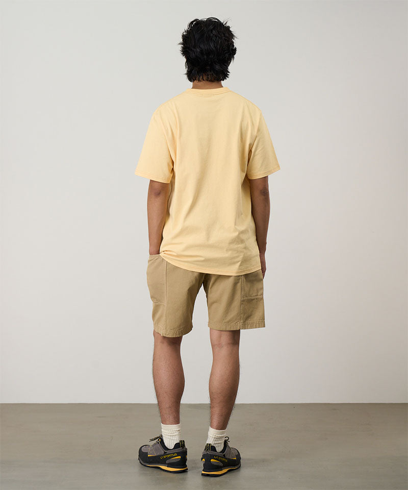 Back view of a model wearing a mango Gramicci G-Flower Tee with a sunflower graphic and beige shorts on a light tone background.