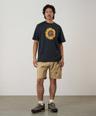 Model wearing a vintage black Gramicci G-Flower Tee with a sunflower graphic and beige shorts on a light tone background.