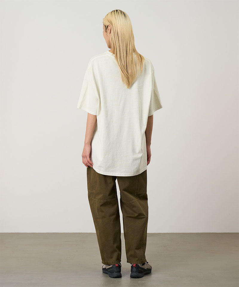 Back view of a model wearing a natural pigment Gramicci Freedom Tee Pigment Dyed and brown pants on a light tone background.
