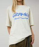 Model wearing a Gramicci natural pigment Freedom Tee Pigment Dyed with blue graphic against a light tone background.