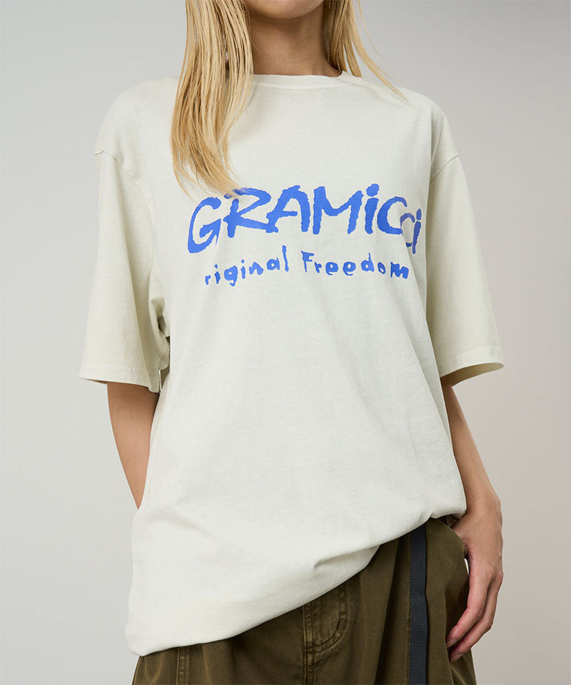Model wearing a Gramicci natural pigment Freedom Tee Pigment Dyed with blue graphic against a light tone background.