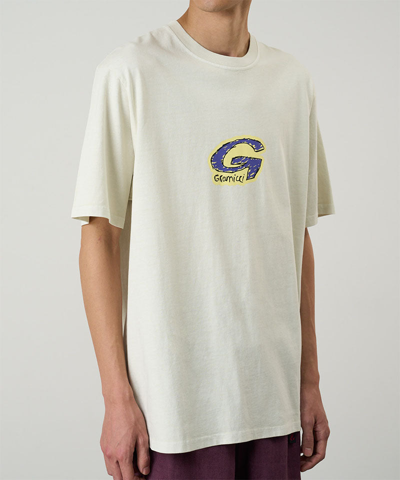 Model wearing a Gramicci natural colored G-Scribble Tee Pigment Dyed shirt with purple graphic against a light tone background.
