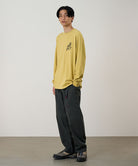 Model wearing a sulpher pigment Gramicci Running Man L/S Tee Pigment Dyed with a grey graphic and dark pants on a light-tone background.