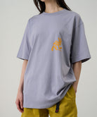 Person wearing a light purple t-shirt with a yellow logo on a plain background