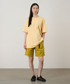 Person wearing a yellow t-shirt and shorts standing against a plain background