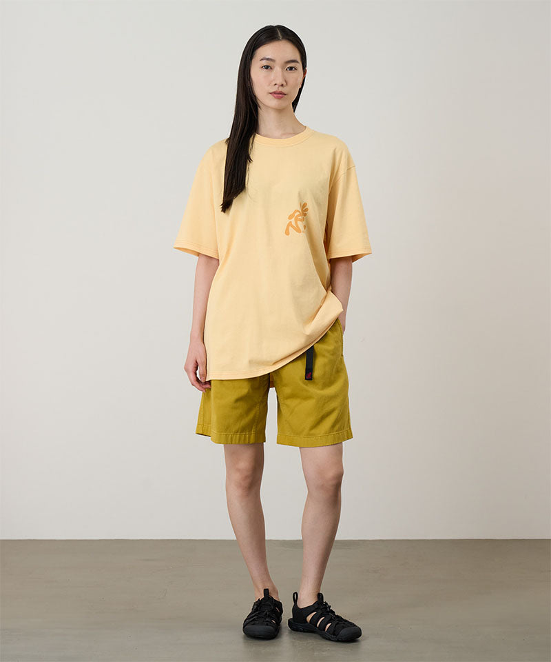 Person wearing a yellow t-shirt and shorts standing against a plain background