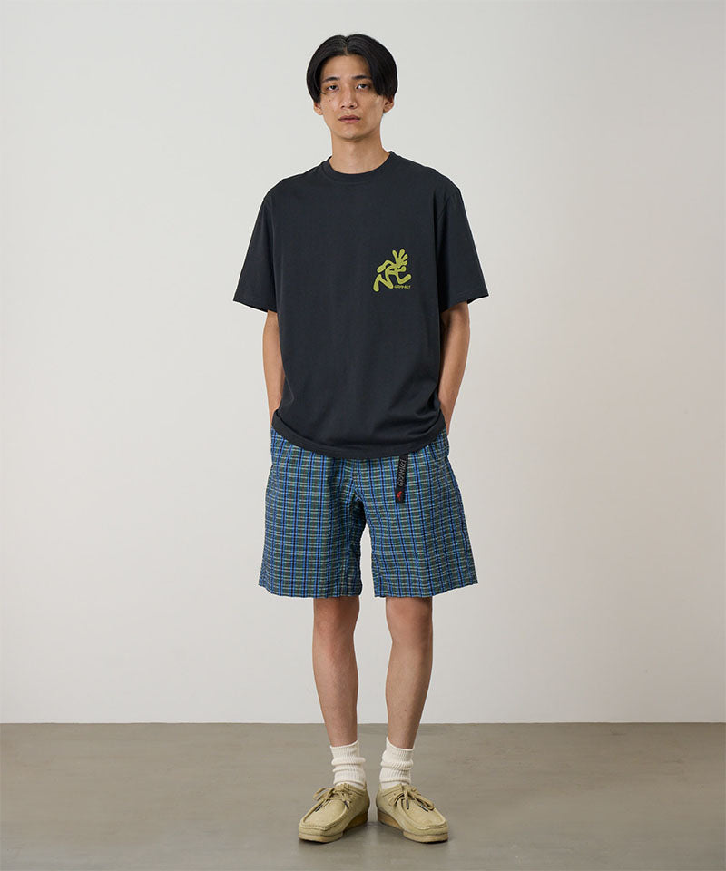 Person wearing a black t-shirt with a yellow logo and plaid shorts on a plain background