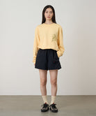 Model wearing a mango colored Gramicci Sticky Hands L/S Tee with a green frog graphic and black shorts on a light tone background.