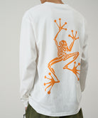 Model wearing a Gramicci white Sticky Hands L/S Tee with orange frog graphic against a light tone background.