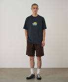 Model wearing a vintage black Gramicci Turtle Tee with a a turtle graphic and brown shorts on a light tone background.
