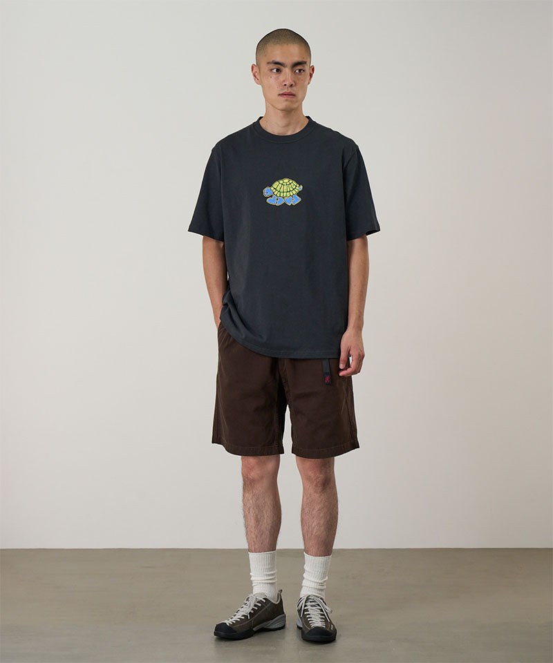 Model wearing a vintage black Gramicci Turtle Tee with a a turtle graphic and brown shorts on a light tone background.
