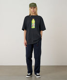 Model wearing a vintage black Gramicci Quencher Tee with a hydration drink graphic and blue pants on a light tone background.