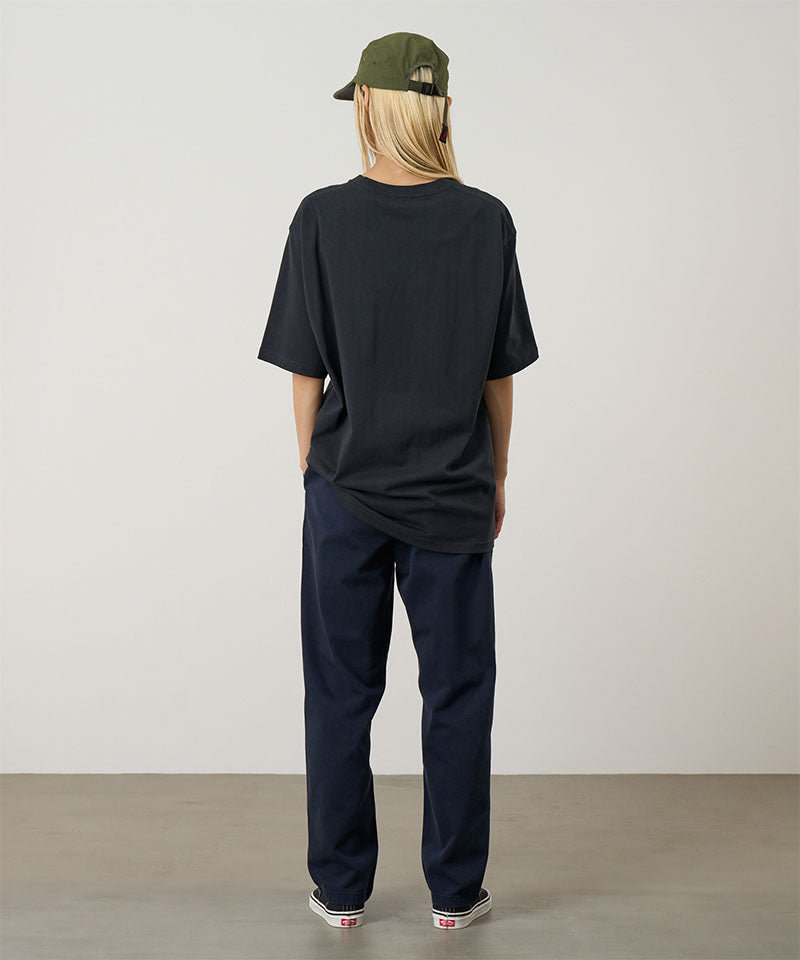 Rear view of a model wearing a vintage black Gramicci Quencher Tee and blue pants on a light tone background.