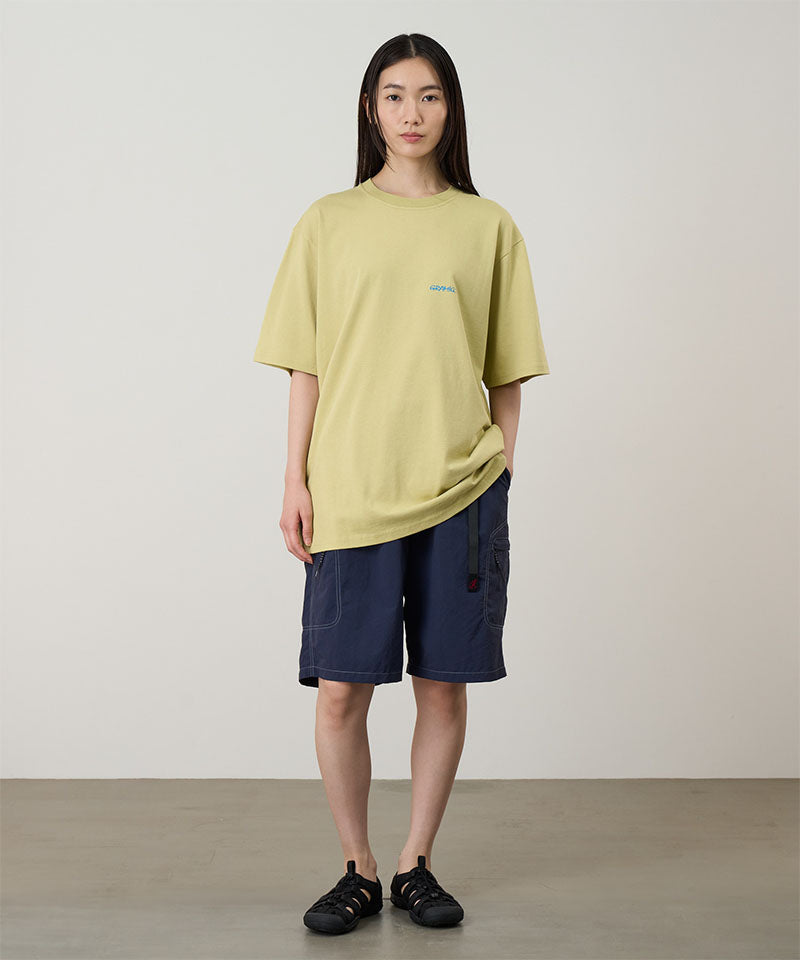 Model wearing a lime colored Gramicci Ice Sculpture Tee with Gramicci branding and blue shorts on a light tone background.