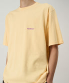 Model wearing a Gramicci mango colored Ice Sculpture Tee with graphic against a light tone background.