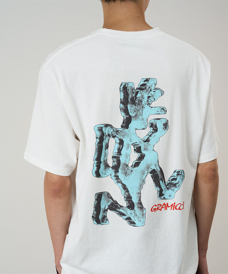 Back view of a model wearing a Gramicci white Ice Sculpture Tee with a running man graphic against a light tone background.