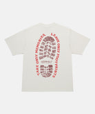 Back view of a Gramicci natural pigment Footprints Tee Pigment Dyed with red graphic against a light tone background.