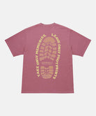 Back view of a Gramicci red pigment Footprints Tee Pigment Dyed with yellow graphic against a light tone background.