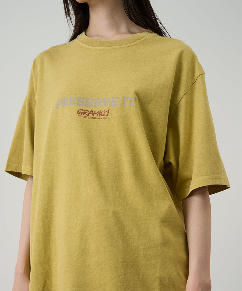 Model wearing a Gramicci sulphur pigment Footprints Tee Pigment Dyed with grey graphic against a light tone background.