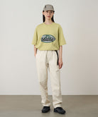 Model wearing a lime green Gramicci Half Dome Tee with a grey and green graphic and light beige pants on a light tone background.
