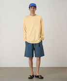 Person wearing a yellow long-sleeve shirt, blue cap, and plaid shorts on a plain background