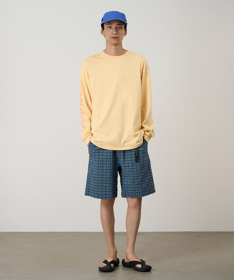 Person wearing a yellow long-sleeve shirt, blue cap, and plaid shorts on a plain background