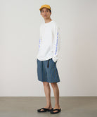 Person wearing a white long-sleeve shirt with blue text and plaid shorts on a plain background