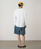 Person wearing a white long-sleeve shirt and blue plaid shorts with a yellow cap on a plain background