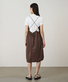 Back view of a model wearing a Gramicci Women's Woven Milton Dress in the color walnut and a white undershirt on a light-tone background.
