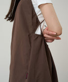 Model wearing a Gramicci Women's Woven Milton Dress in the color walnut and a white undershirt on a light-tone background.

