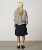Back view of a model wearing black Gramicci Guide Skort and a beige jacket on a light-tone background.