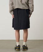 Back view of a model wearing black Gramicci Guide Skort and a beige jacket on a light-tone background.