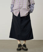 Person wearing a plaid shirt, black skirt, and hiking shoes on a plain background