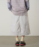 Person wearing a plaid shirt, light gray skirt, and black shoes on a plain background