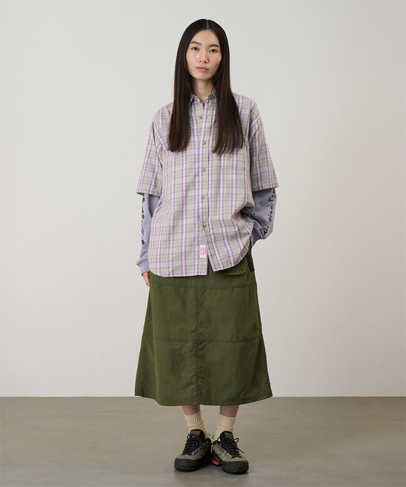 Person wearing a plaid shirt over a long green skirt on a plain background