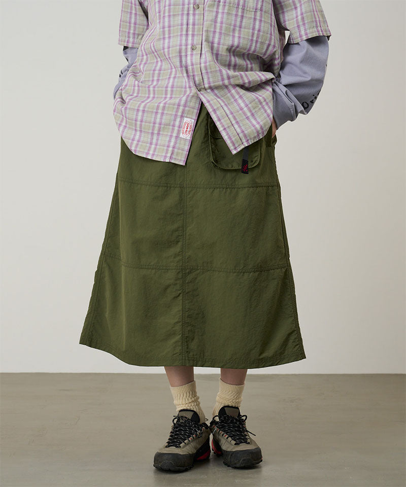 Person wearing a green skirt, plaid shirt, and hiking boots on a plain background