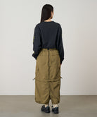 Back view of a model wearing a Gramicci Convertible Cargo Skirt in the color khaki and a black shirt on a light-tone background.