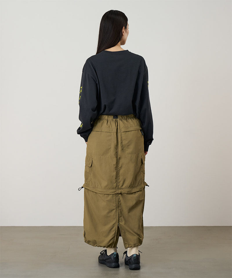 Back view of a model wearing a Gramicci Convertible Cargo Skirt in the color khaki and a black shirt on a light-tone background.