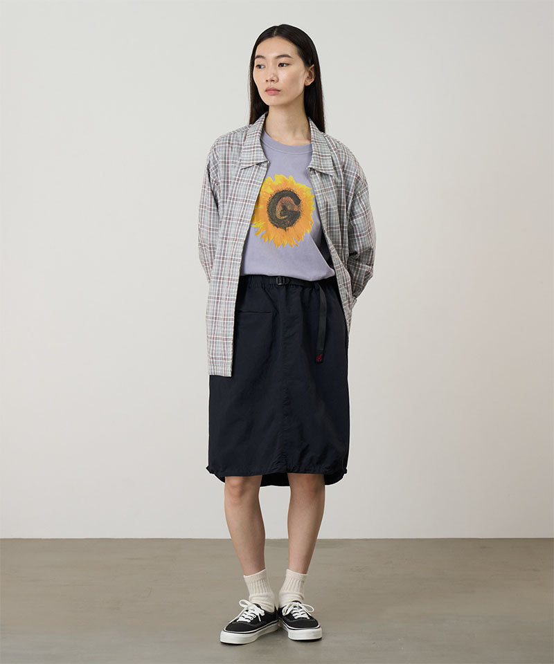 Person wearing a plaid shirt over a graphic t-shirt with a sunflower design, black skirt, and sneakers on a plain background.
